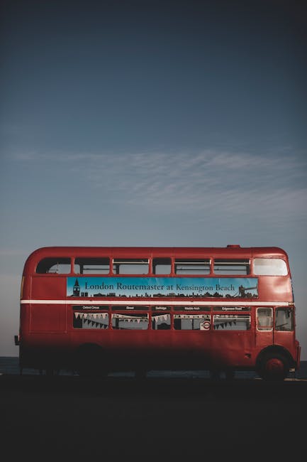 A red double-decker bus parked outdoors, with the upper deck filled with Windows and the lower deck featuring a large advertising panel for London's Routemaster buses at Kensington Beach. The bus is p